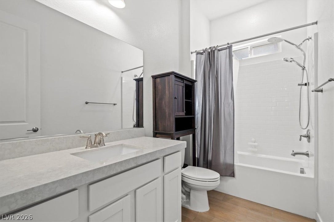 Gleaming tile surrounds the tub alongside a modern vanity and warm wood-look flooring.