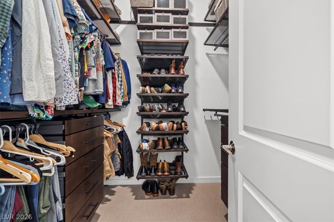 An organized walk-in closet features built-in storage systems and neutral carpeted flooring.