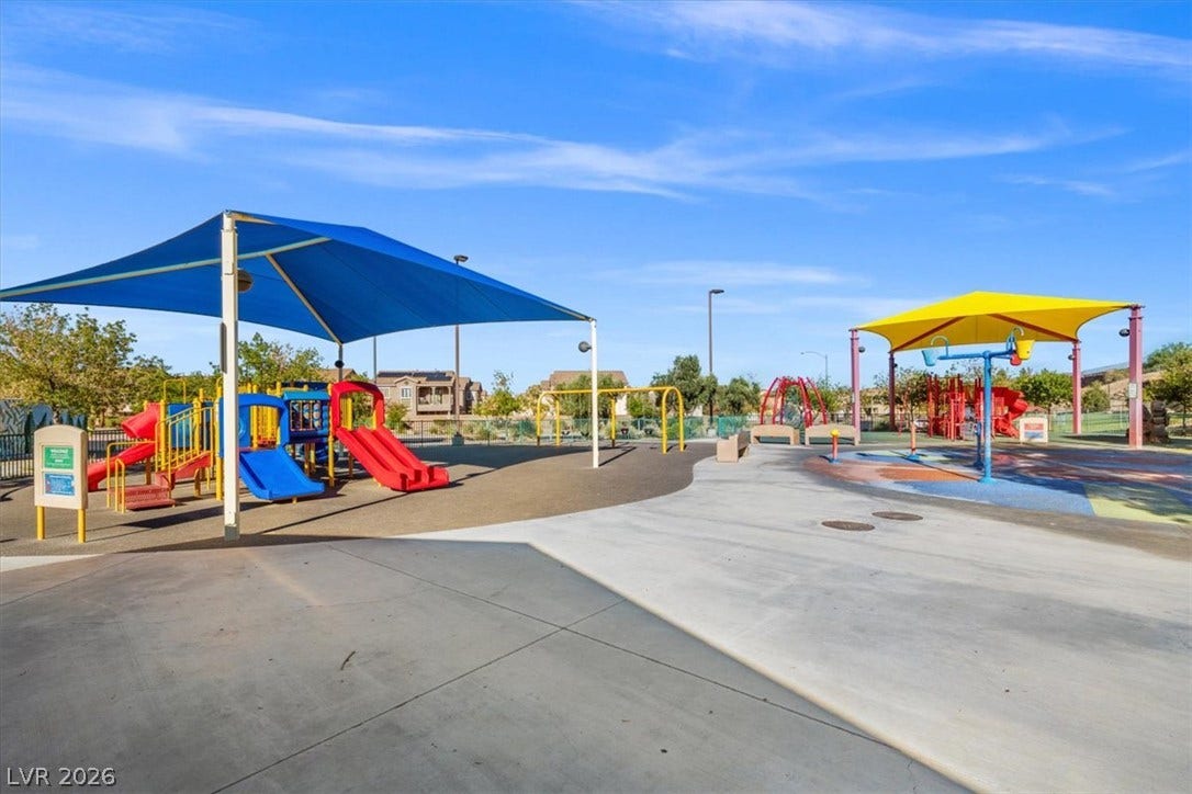A well-equipped community recreation area features shaded play structures under clear blue skies.