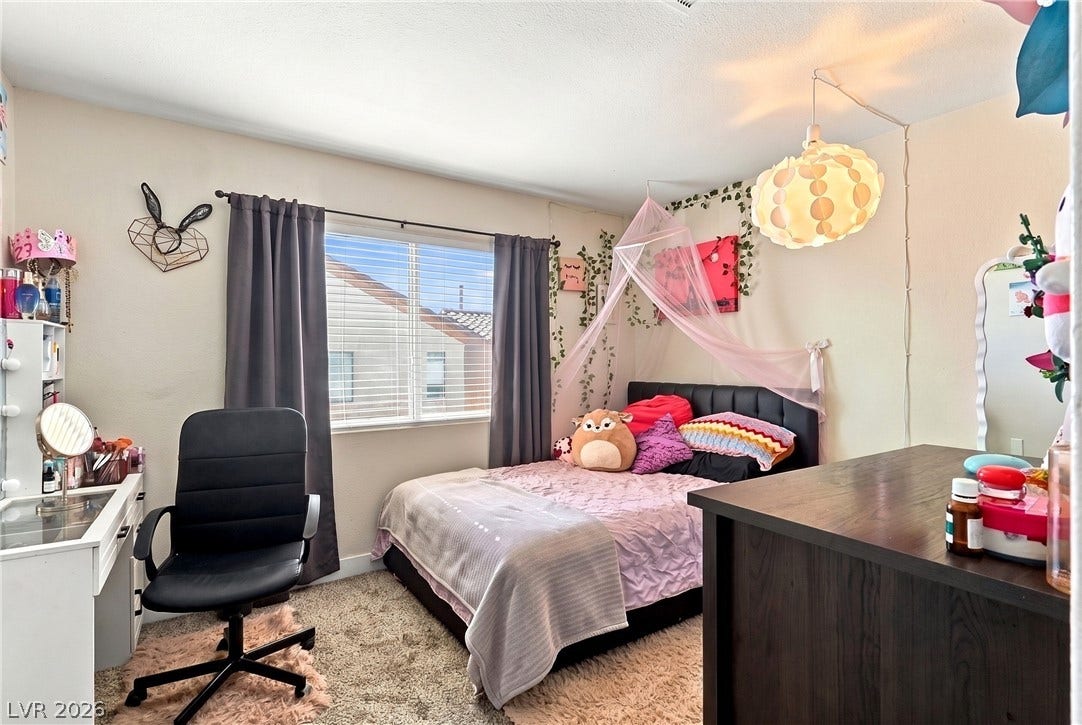 Natural light pours through a large window onto soft carpeting in this cozy bedroom.