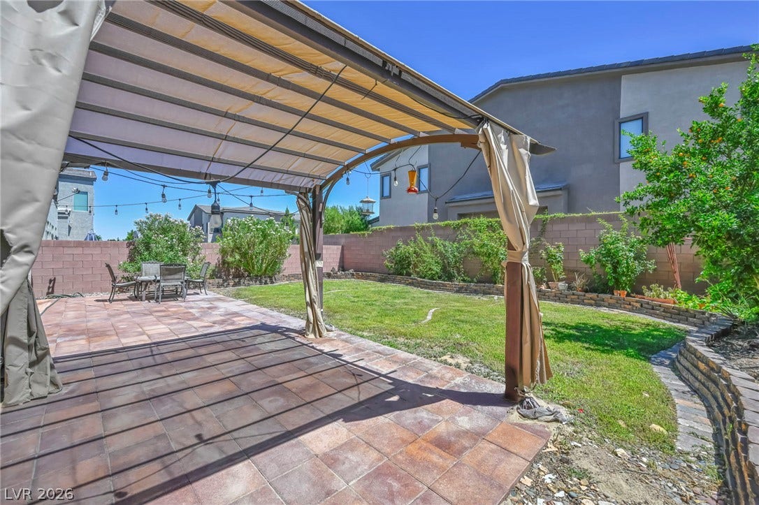 6571 Tangled Vines Avenue, Las Vegas, NV 89139 A spacious backyard features a tiled patio, covered pergola, and a lush grassy lawn.