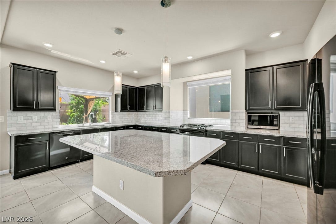 6571 Tangled Vines Avenue, Las Vegas, NV 89139 Polished stone countertops and generous dark cabinetry anchor this light-filled modern kitchen.