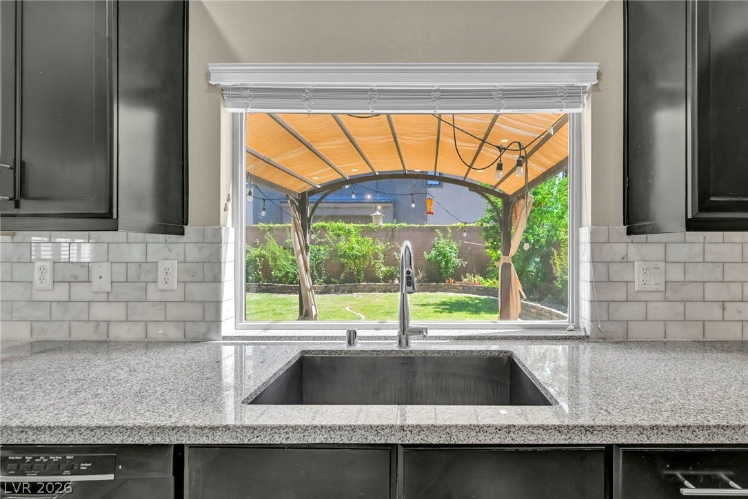 6571 Tangled Vines Avenue, Las Vegas, NV 89139 A wide kitchen window frames views of the backyard lawn and shaded patio area.