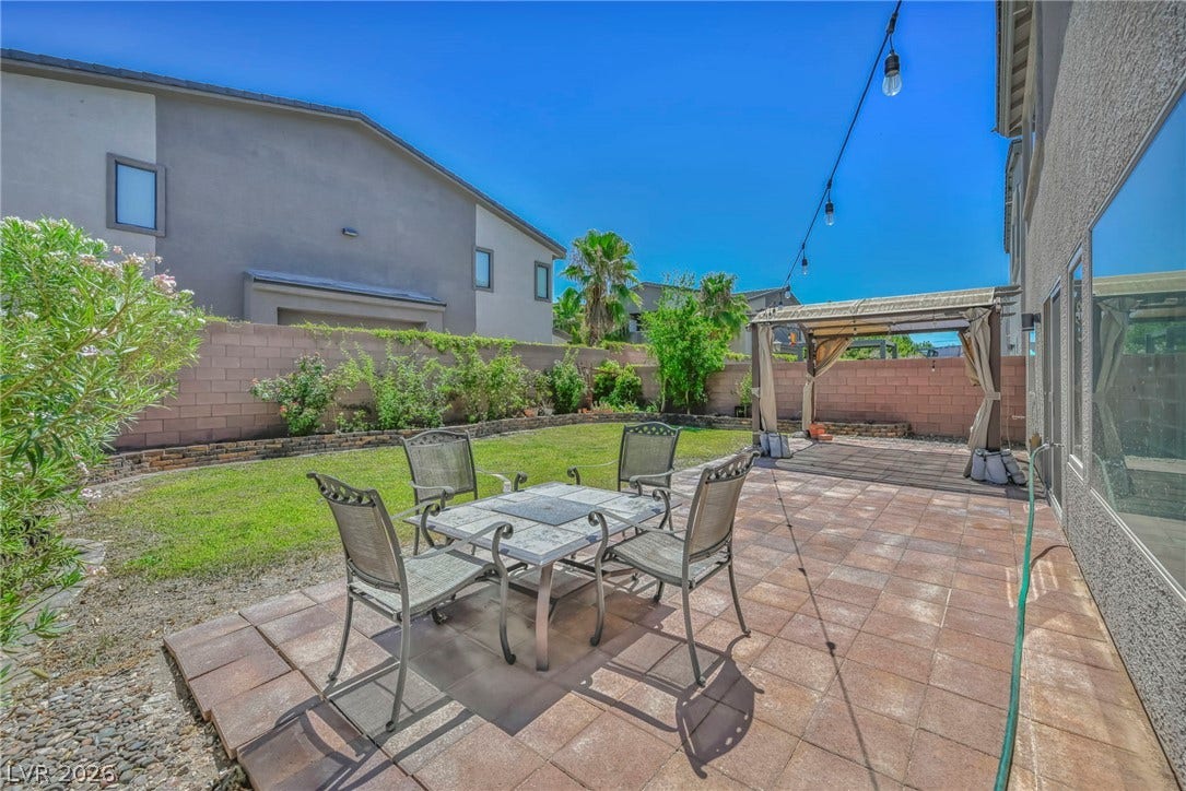 6571 Tangled Vines Avenue, Las Vegas, NV 89139 Tiled backyard patio borders a grassy lawn enclosed by high privacy walls.