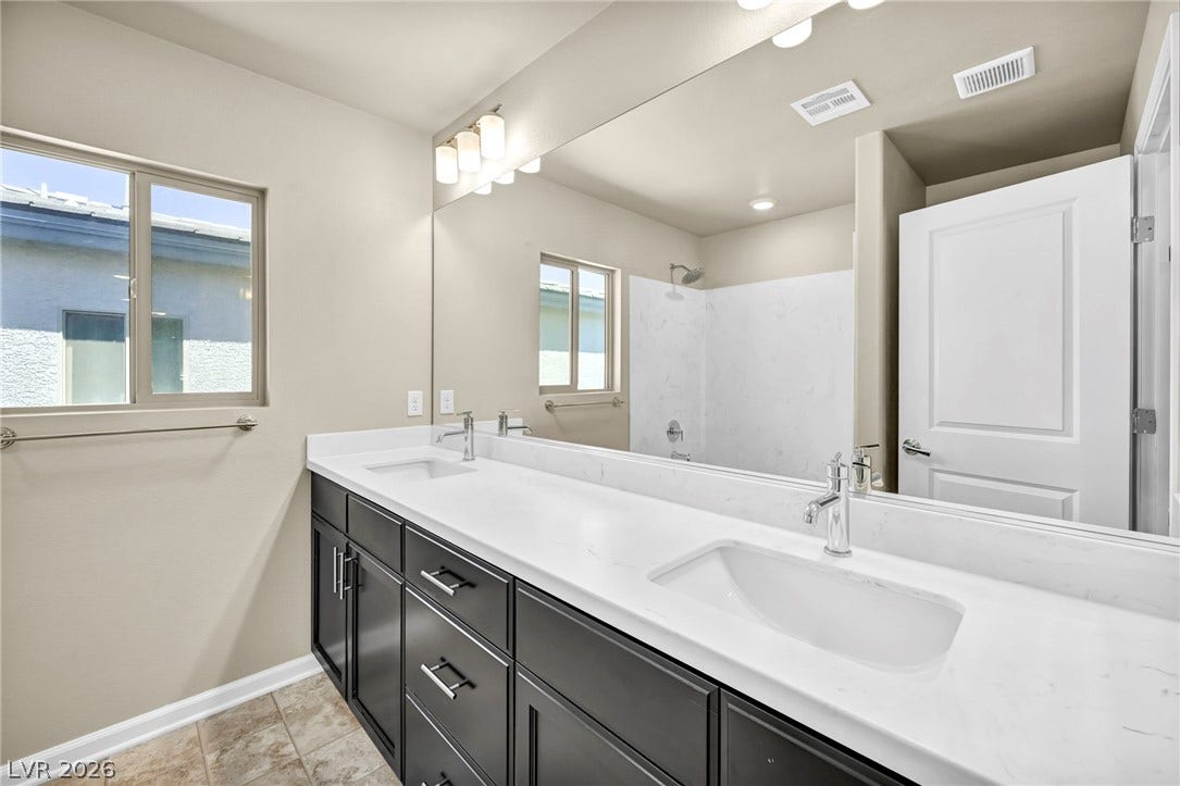 6571 Tangled Vines Avenue, Las Vegas, NV 89139 Double vanities with stone counters flank a spacious, modern bathroom layout.