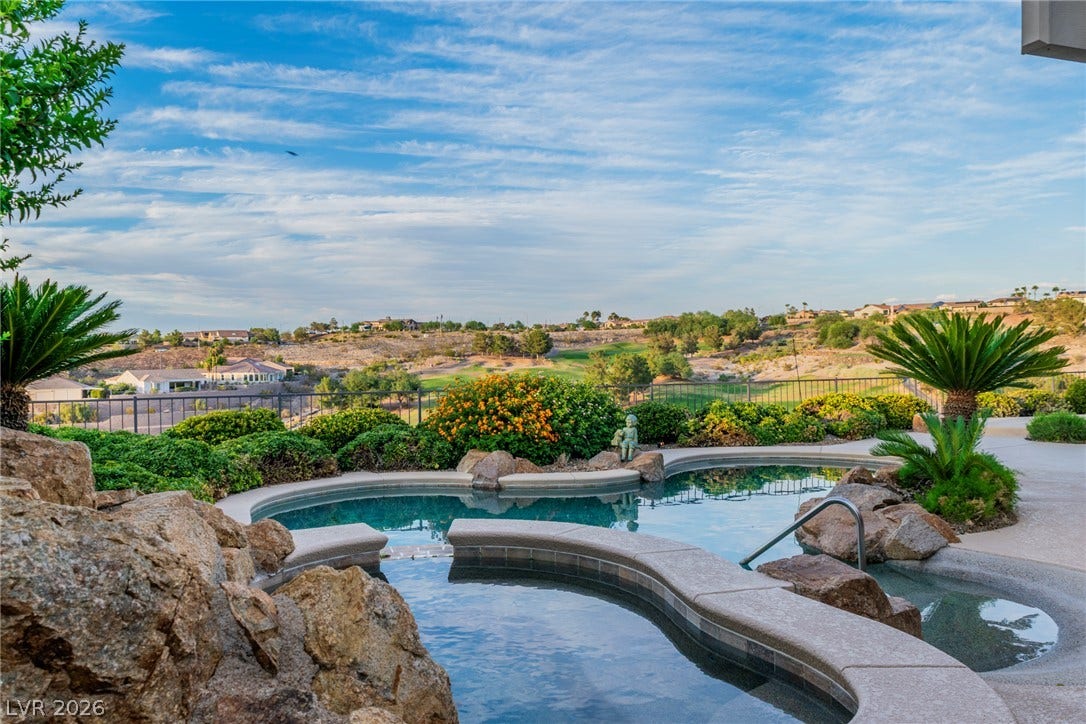 2734 Cherrydale Falls Drive, Henderson, NV 89052 A sparkling freeform pool overlooks rolling hills and a manicured golf course under blue skies.