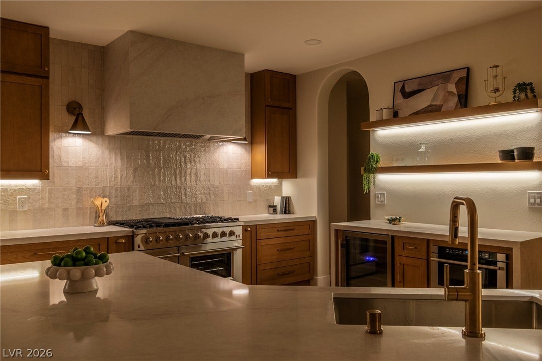2734 Cherrydale Falls Drive, Henderson, NV 89052 Rich wood cabinetry and stone countertops elevate this kitchen, illuminated by subtle under-cabinet lighting.
