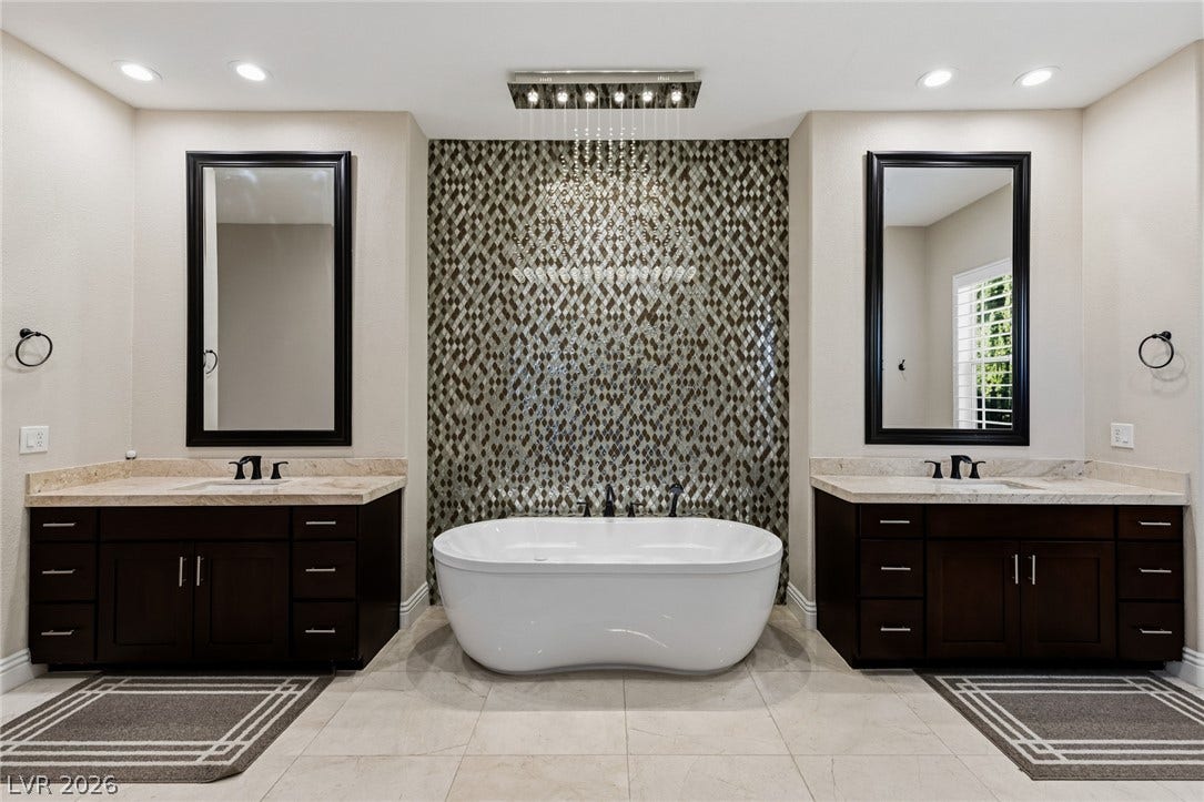 204 Satin Mist Court, Las Vegas, NV 89144 A freestanding tub sits centered between two elegant dark wood vanities on tiled flooring.