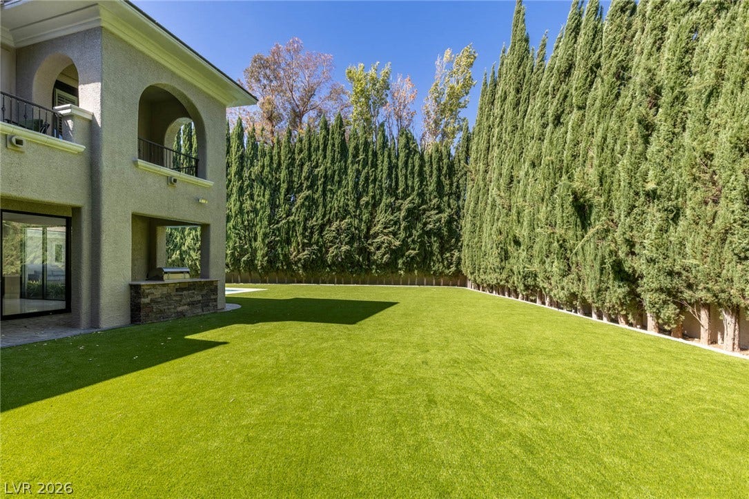 204 Satin Mist Court, Las Vegas, NV 89144 Manicured green turf stretches alongside a towering hedge of cypress trees bordering the stone exterior.