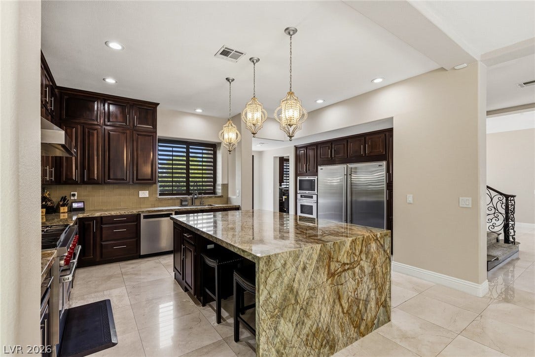 204 Satin Mist Court, Las Vegas, NV 89144 Gleaming stone countertops and dark wood cabinetry anchor this spacious modern kitchen with large tile flooring.
