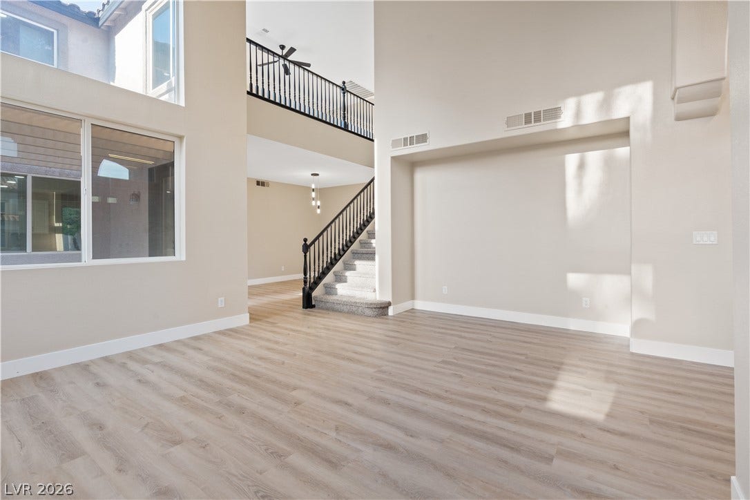 1662 Ravanusa Drive, Henderson, NV 89052 Double-height ceilings and tall windows illuminate a spacious main living area with modern plank flooring.