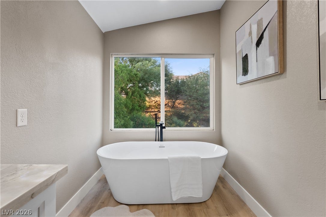 1662 Ravanusa Drive, Henderson, NV 89052 A modern soaking tub rests beneath a large window framing leafy green views.