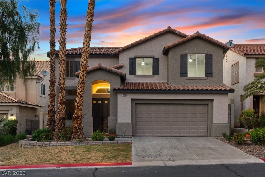 1662 Ravanusa Drive, Henderson, NV 89052 Stately stucco architecture rises behind towering palms, anchoring a concrete driveway and two-car garage.