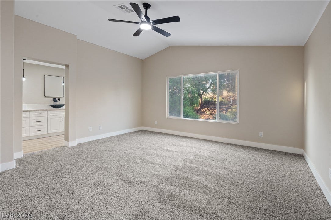 1662 Ravanusa Drive, Henderson, NV 89052 A spacious bedroom features plush carpeting, vaulted ceilings, and views of the surrounding trees.