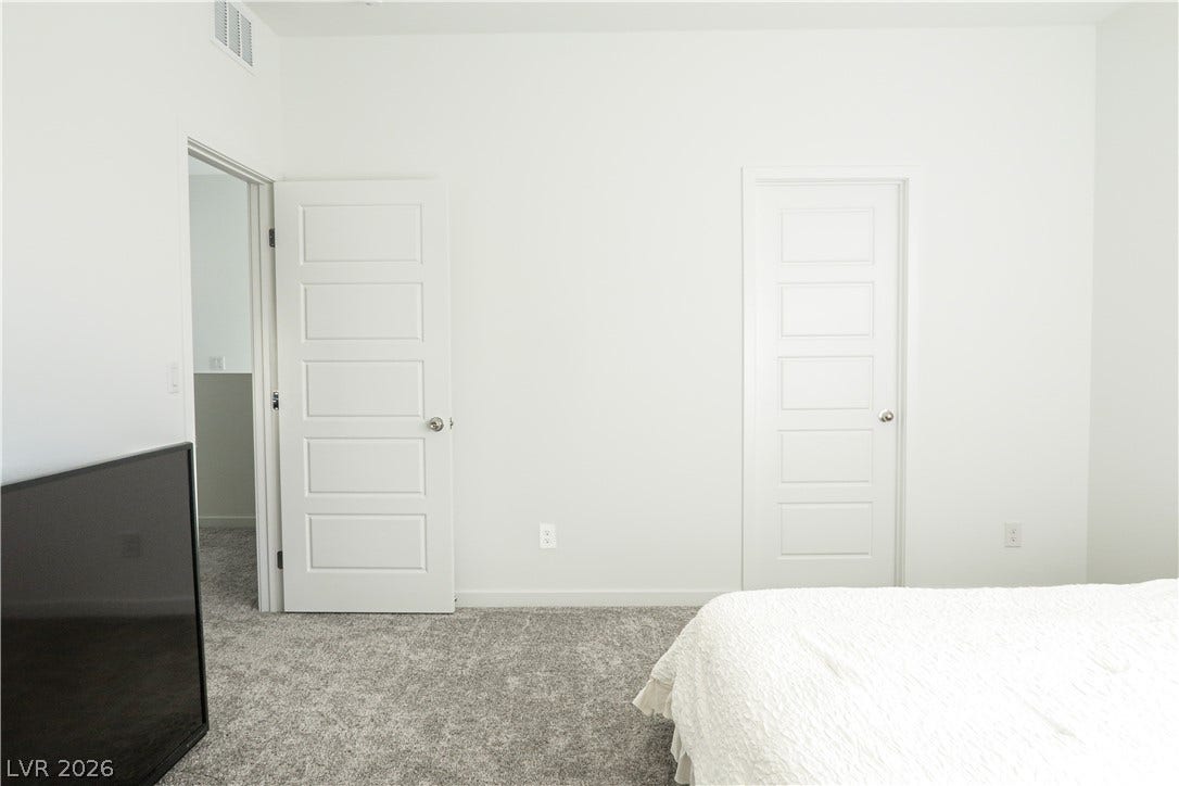 Crisp white walls and soft wall-to-wall carpeting define this serene bedroom space.