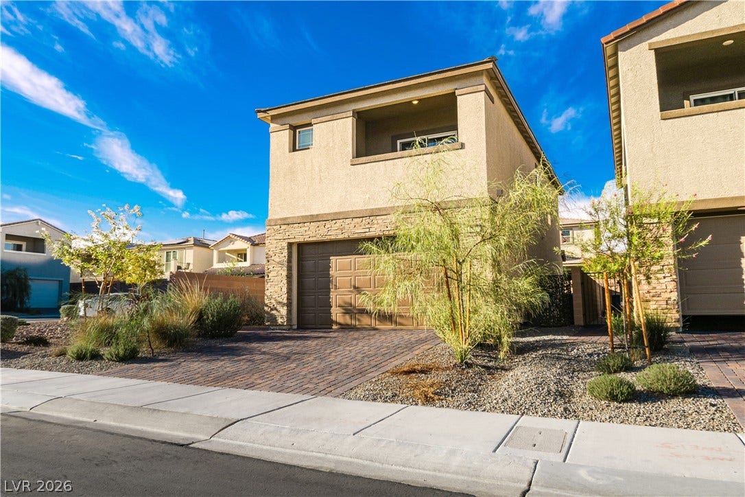 An inviting stone-accented facade stands out alongside a neat paver driveway and desert landscaping.