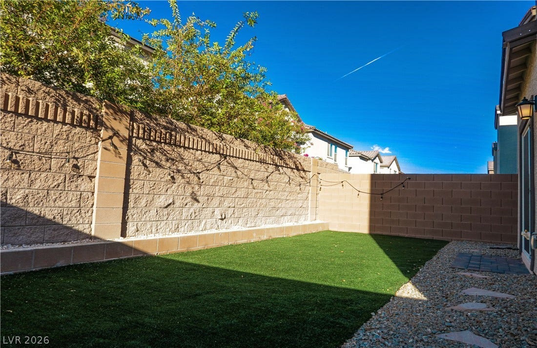 A private backyard features a level lawn bordered by tall block wall fencing.