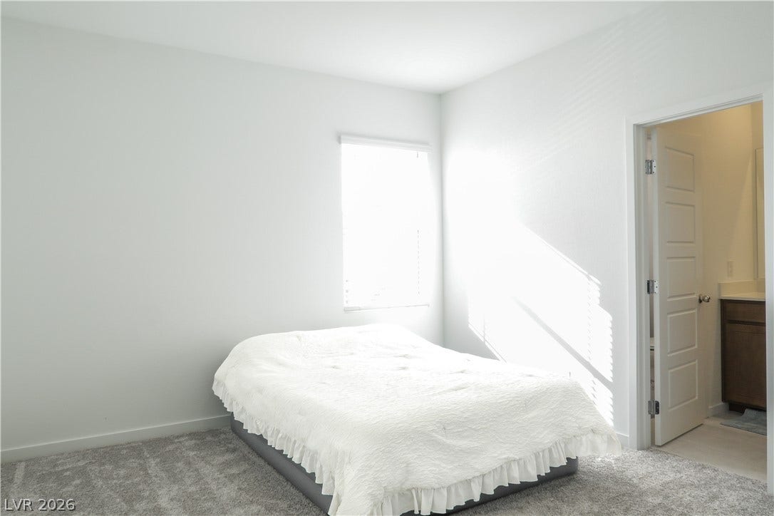 Natural light streams across soft carpeting in this bedroom with an attached bath.