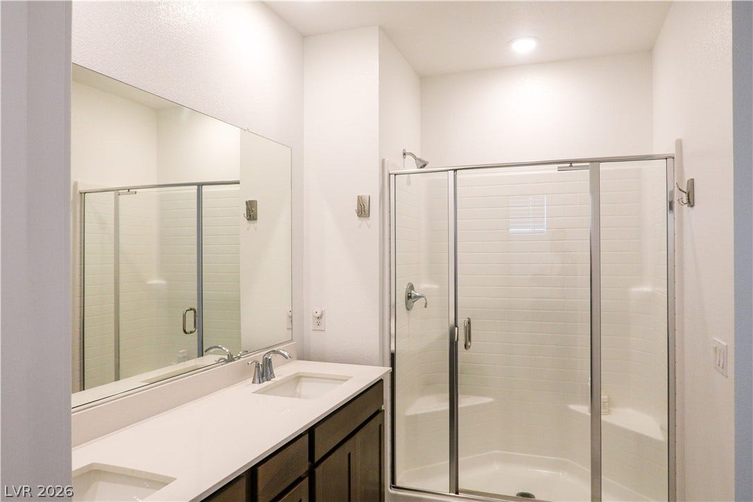 A sleek double vanity sits beside a modern glass-enclosed shower with tile surrounds.