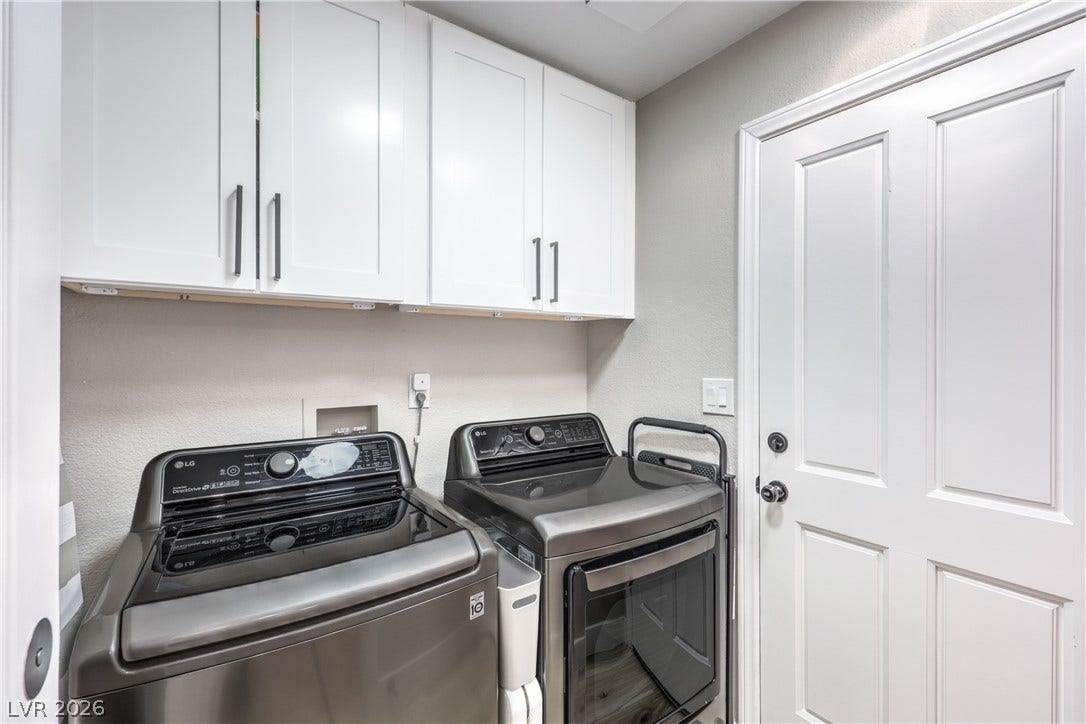 8211 Round Hills Circle, Las Vegas, NV 89113 This organized utility space features white cabinetry above a modern washer and dryer set, offering streamlined functionality.