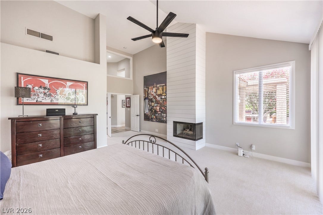 8211 Round Hills Circle, Las Vegas, NV 89113 This spacious bedroom showcases a contemporary fireplace, soft carpeting, and a modern ceiling fan, creating a comfortable retreat.