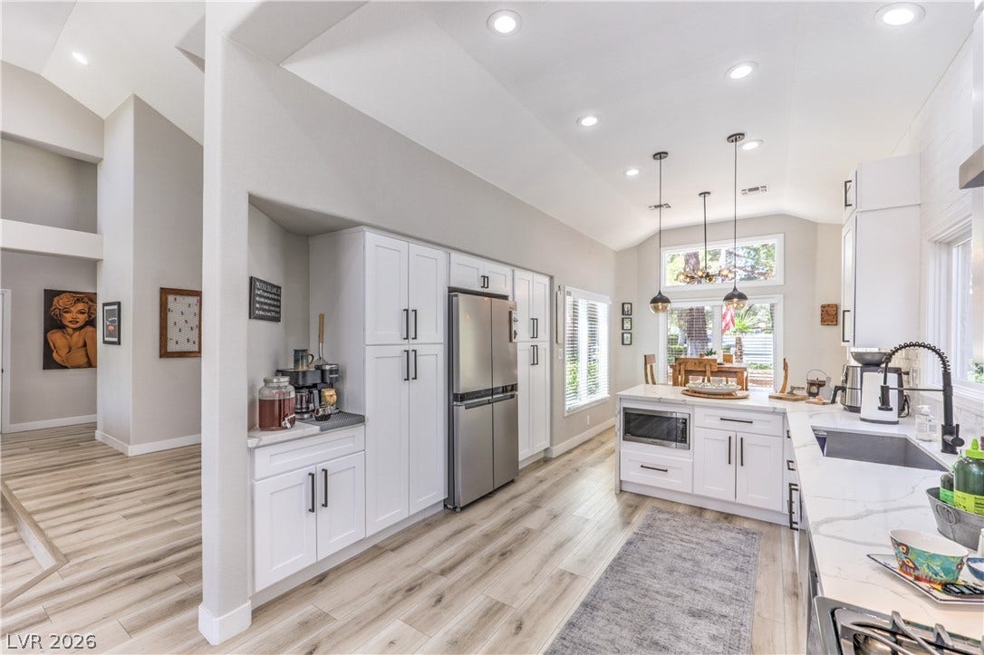 8211 Round Hills Circle, Las Vegas, NV 89113 A luminous kitchen featuring white cabinetry, modern appliances, and a central island with a built-in microwave, complemented by elegant pendant lighting.