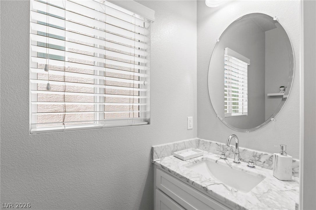 9804 Kodiak Island Court, Las Vegas, NV 89141 An elegant marble-topped vanity stands beneath an oval mirror, illuminated by natural light.