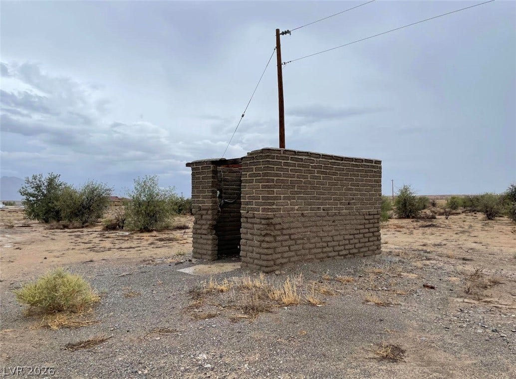 A historic adobe outbuilding stands on a vast desert parcel under wide-open skies.