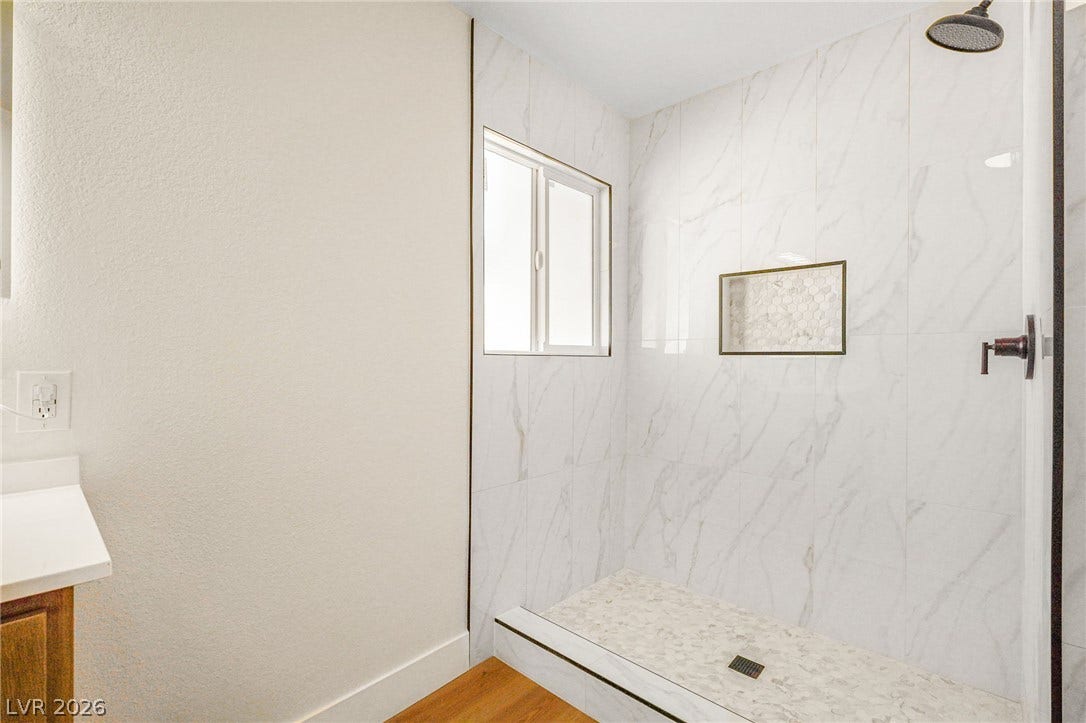 Elegant marble-patterned tile surrounds this modern walk-in shower featuring a built-in storage niche.