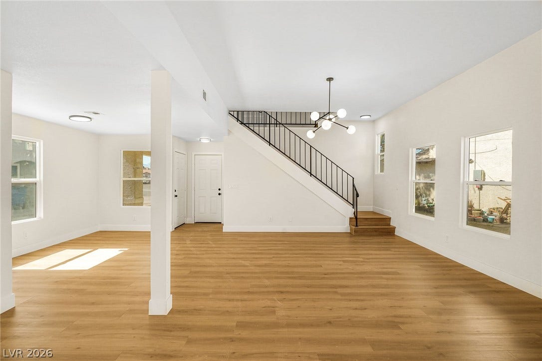 An open floorplan with wood-style flooring leads to a staircase with metal railings.