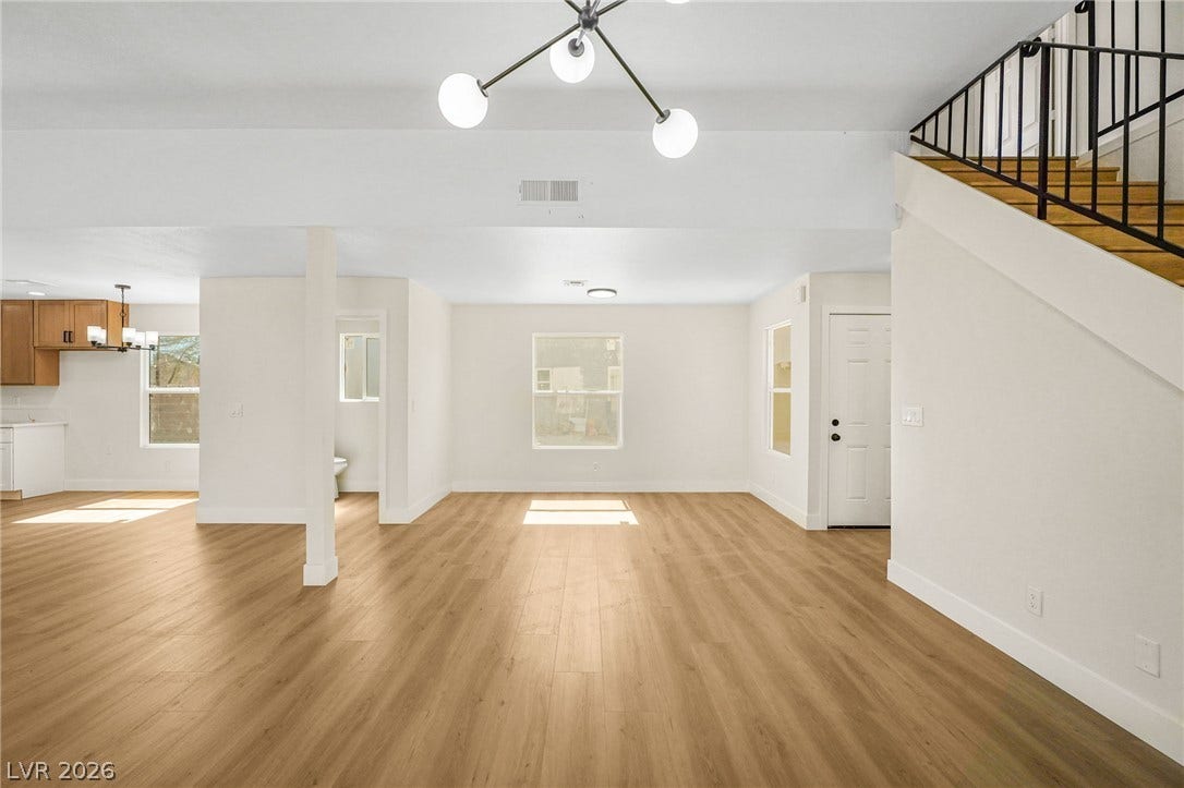 An open floorplan connects versatile living areas with natural wood-toned flooring and crisp white walls.