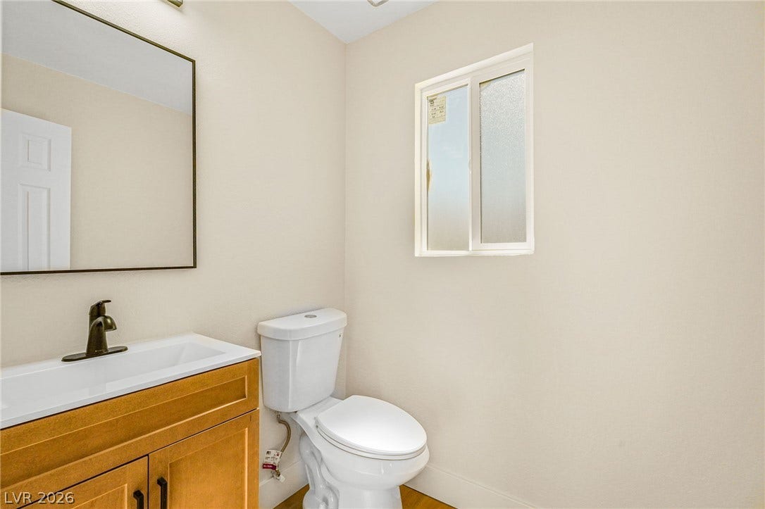 A frosted privacy window illuminates a neutral-toned powder room with a wood vanity.