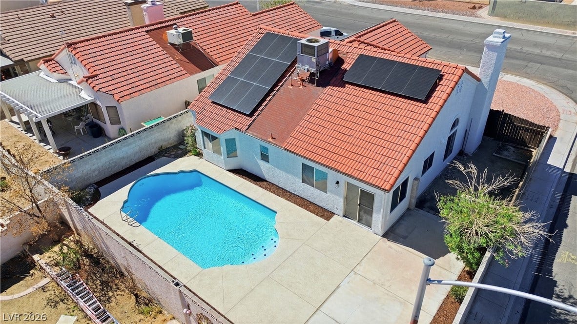 1013 Greystone Drive, Las Vegas, NV 89108 An inviting backyard swimming pool rests adjacent to a tile-roof residence with integrated solar panels.