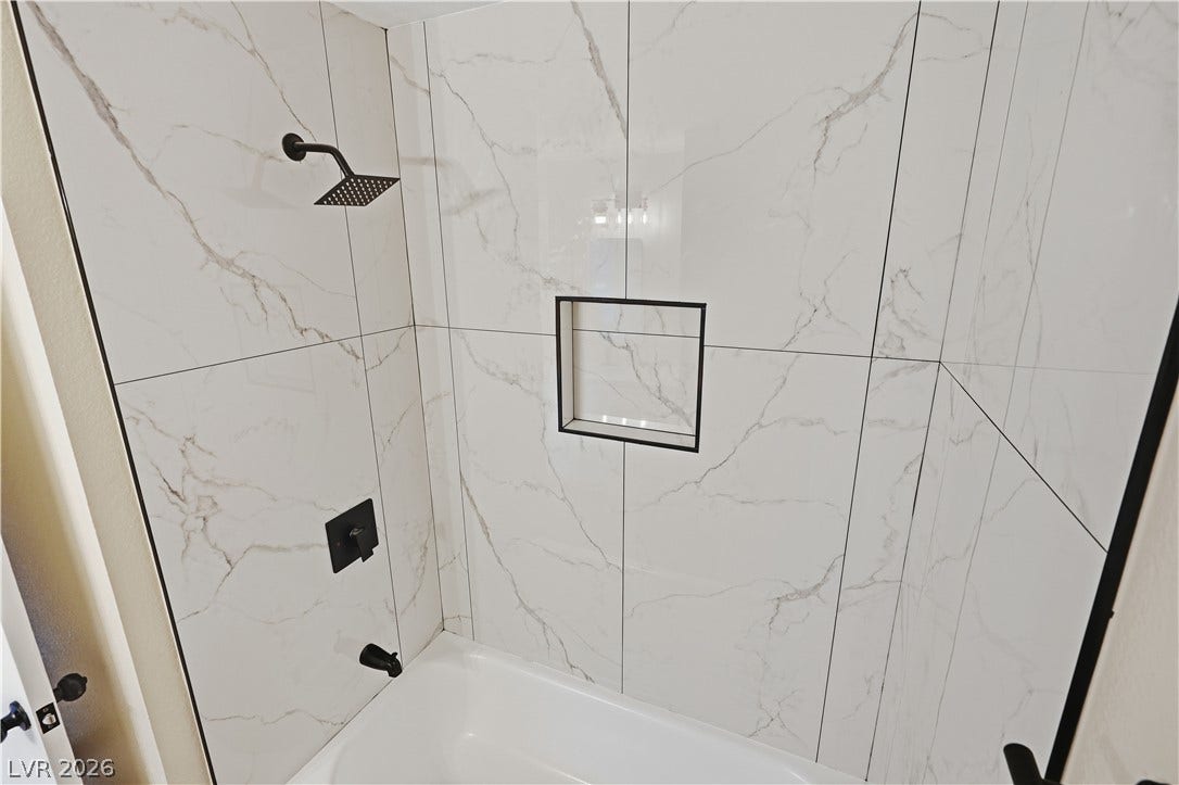 1013 Greystone Drive, Las Vegas, NV 89108 Floor-to-ceiling marble-patterned tile surrounds a deep soaking tub with modern black fixtures.