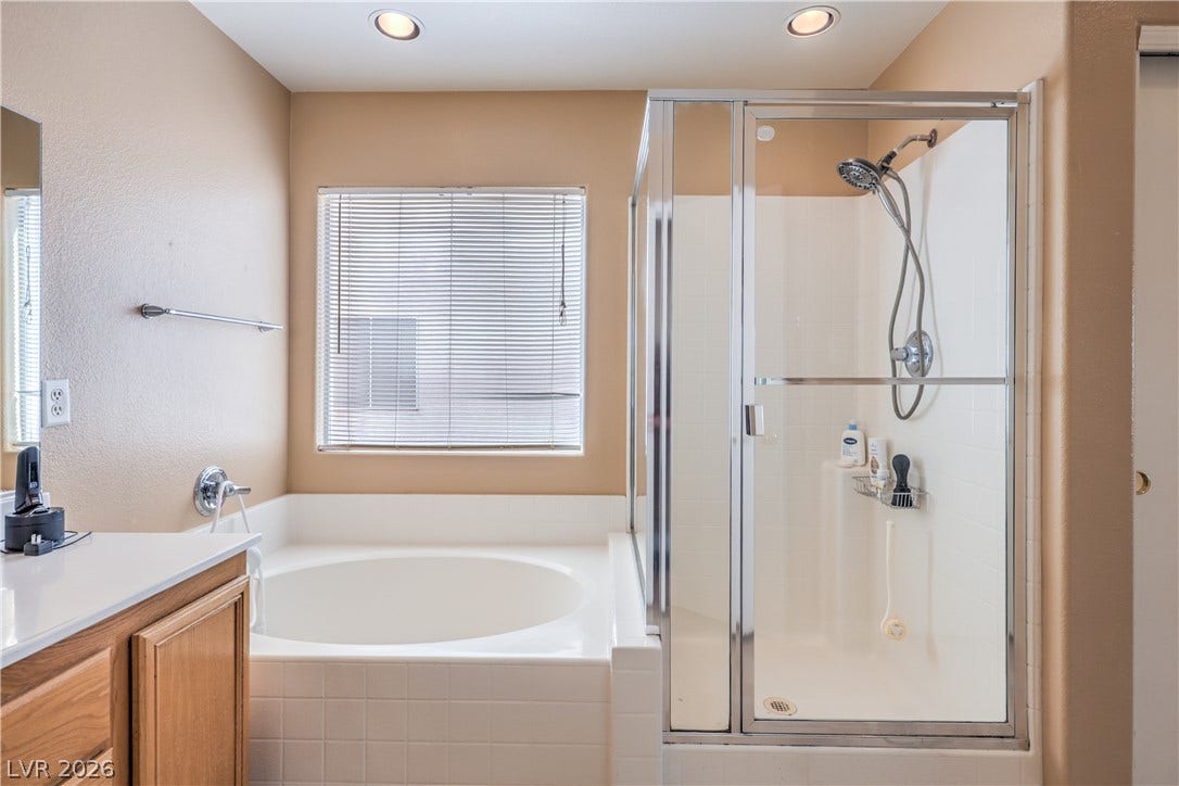 A deep soaking tub sits adjacent to a enclosed walk-in shower under recessed lighting.