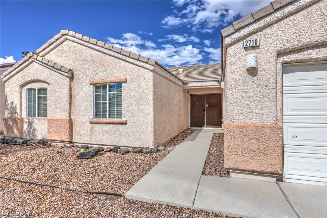 A concrete walkway guides the way to the double-door entrance of this stucco home.