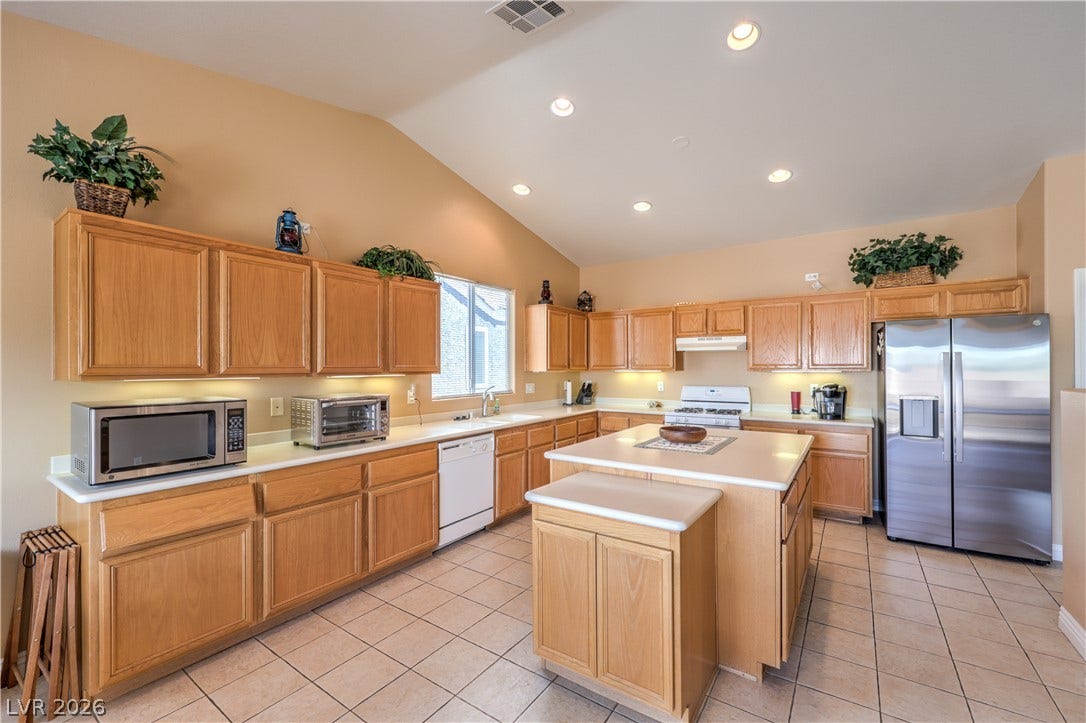 Ample cabinetry and a central island ground this tile-floored kitchen under vaulted ceilings.