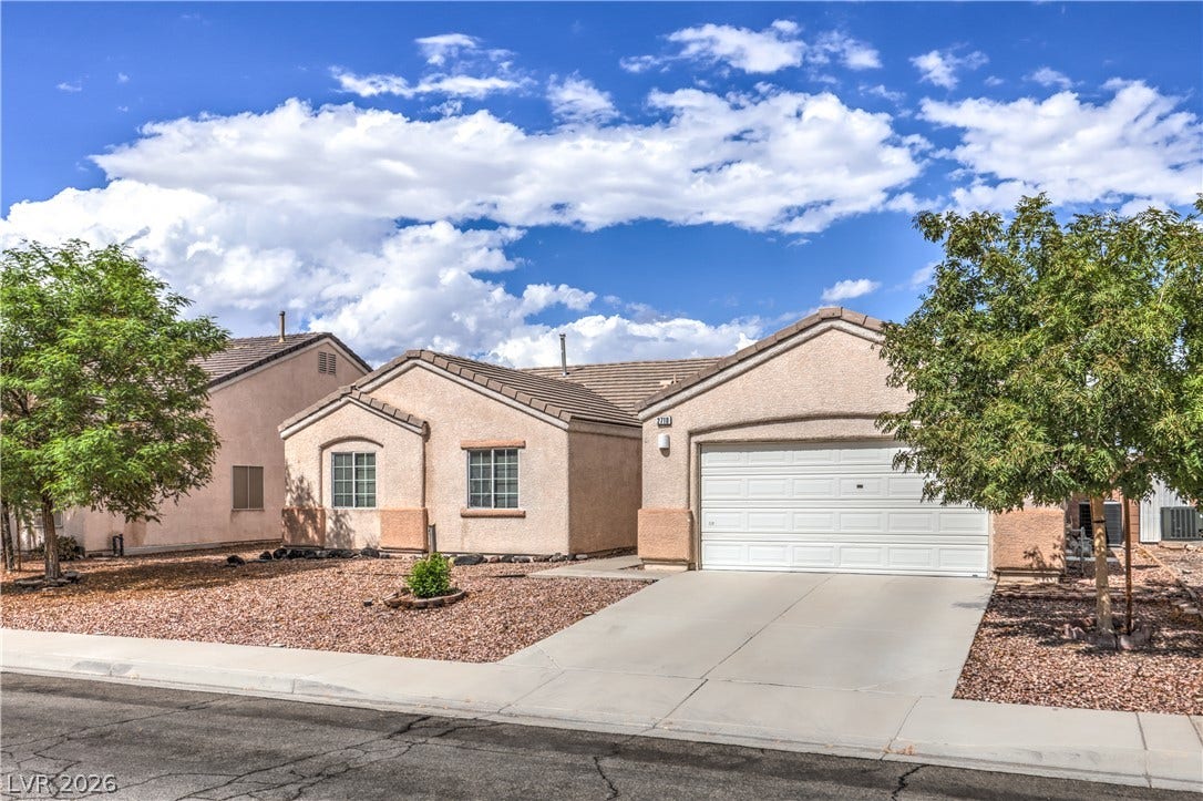 A classic stucco exterior sits behind a low-maintenance desert landscaping with a paved concrete driveway.