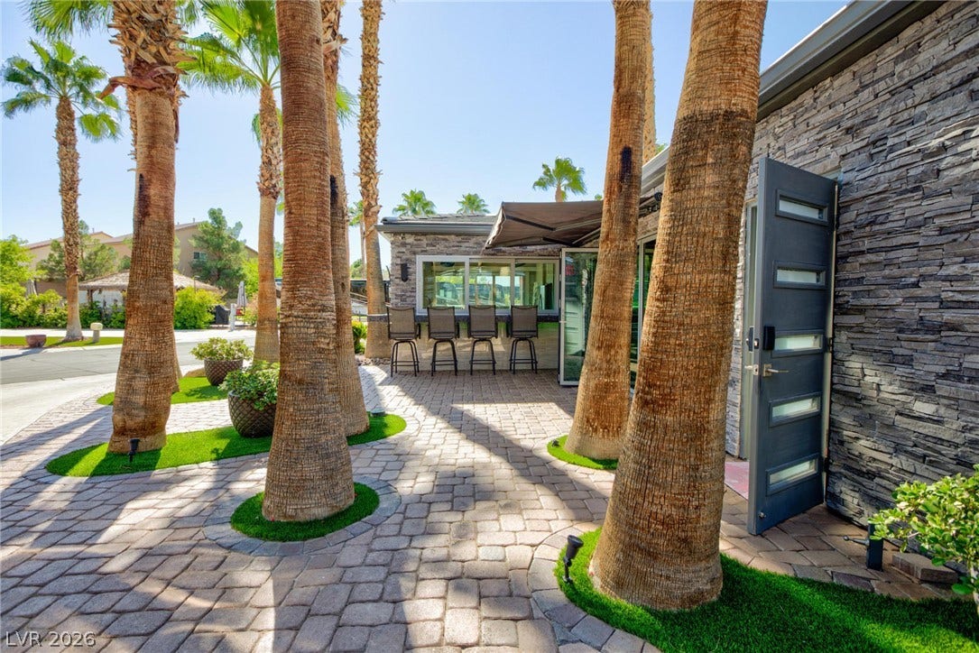 8175 Arville Street, #142, Las Vegas, NV 89139 Mature palm trees frame a paved stone patio and structured stone-clad exterior walls.