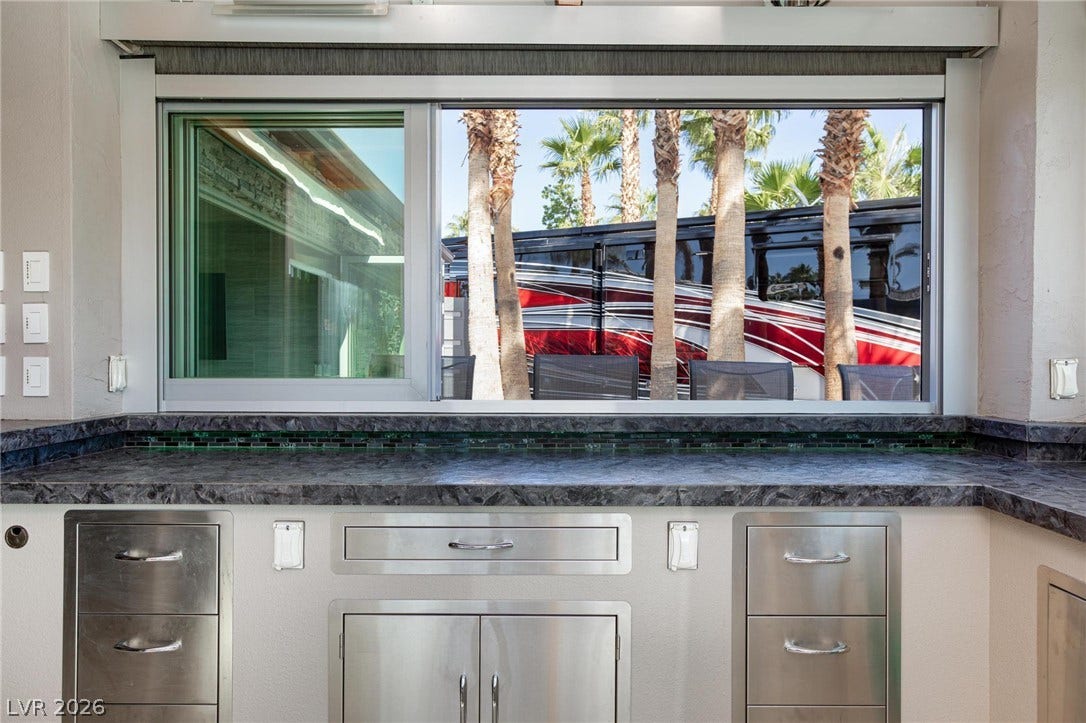8175 Arville Street, #142, Las Vegas, NV 89139 A wide pass-through window opens from the kitchen counter to the palm-lined outdoor living space.
