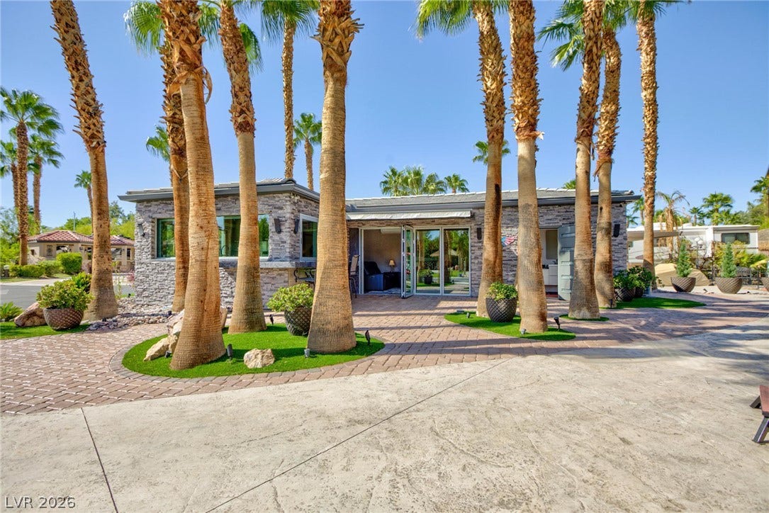 8175 Arville Street, #142, Las Vegas, NV 89139 Lush palm trees and stone-accented exteriors frame a brick-paved patio under clear blue skies.