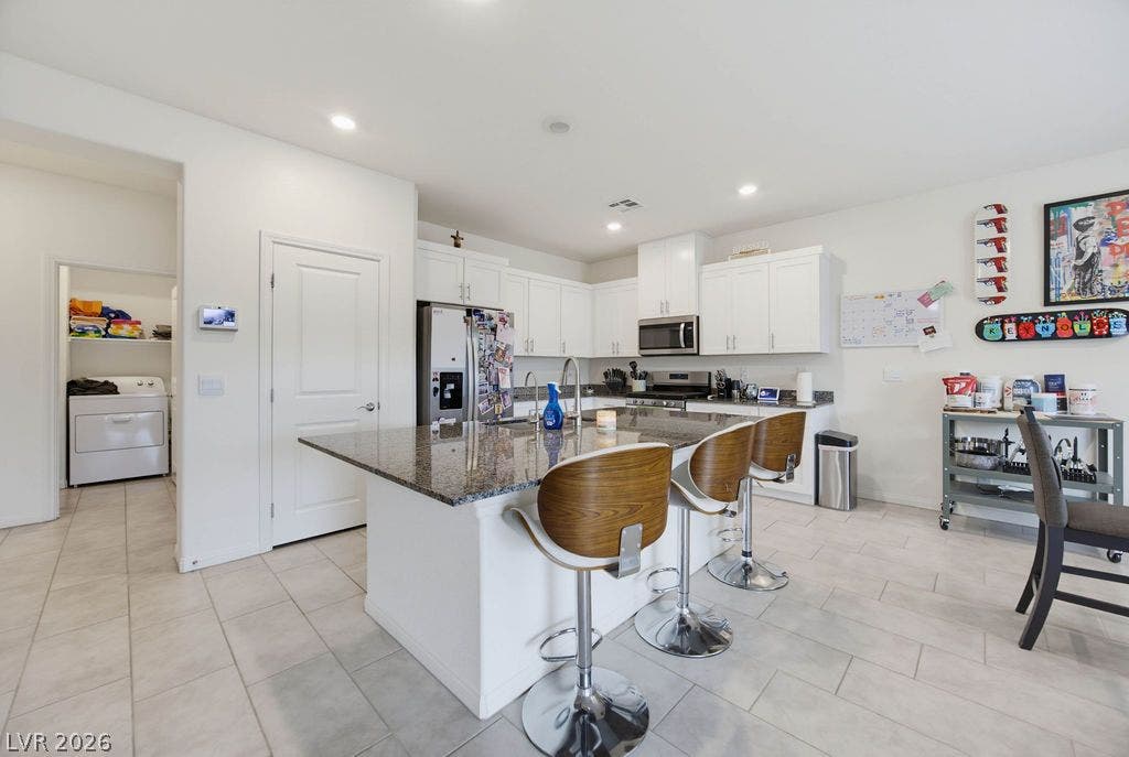 Polished stone counters and white cabinetry define this airy kitchen space featuring durable tile flooring.