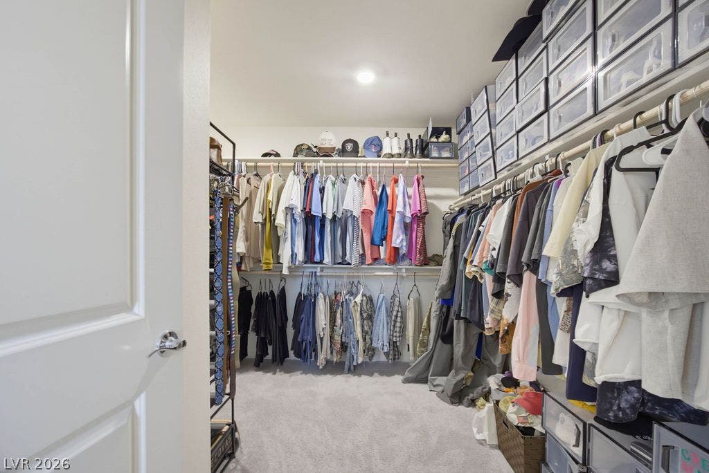 An organized walk-in closet boasts soft neutral carpeting and recessed lighting.