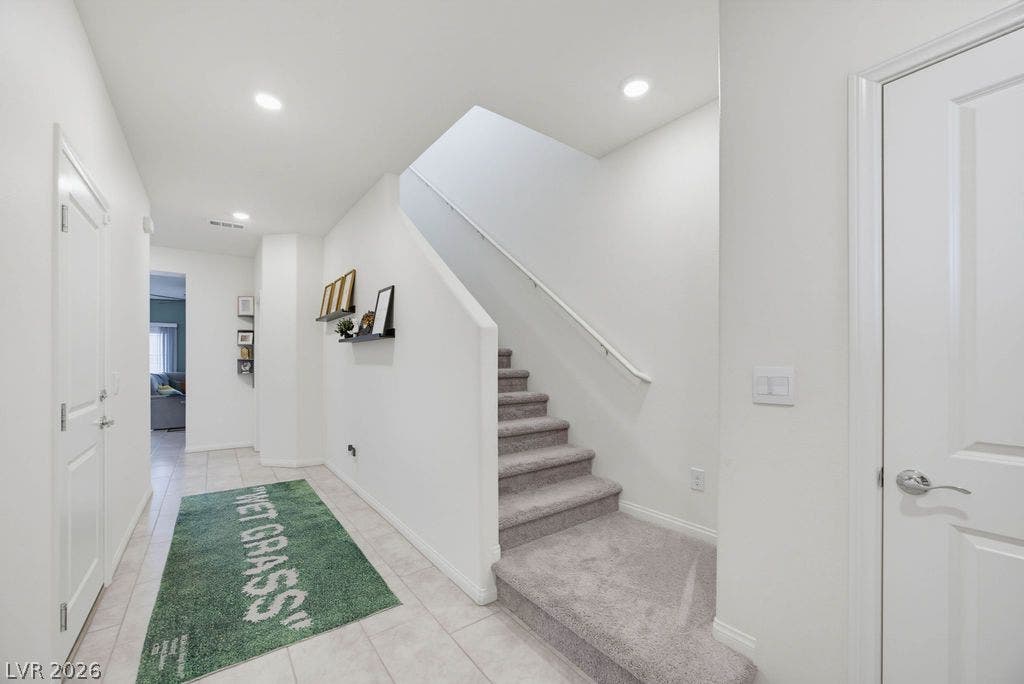 Recessed lighting illuminates this welcoming entry hall leading directly to a carpeted staircase.