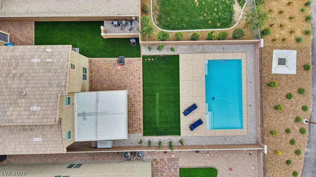 An aerial perspective showcases a backyard pool bordered by neat hardscaping and artificial turf.