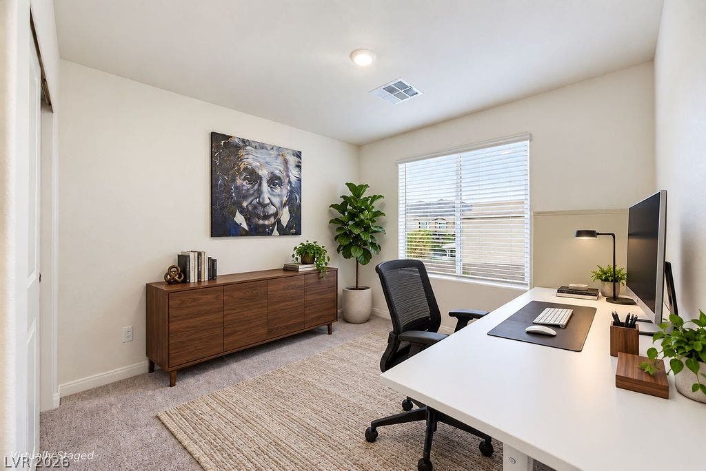A quiet home office features plush carpet and a large window providing ample natural light.