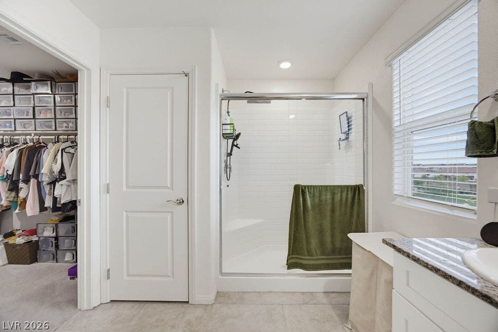 A glass-enclosed shower with subway tile sits adjacent to a walk-in closet.