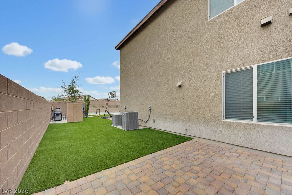 An inviting stone paver patio overlooks a manicured green lawn framed by secure block fencing.