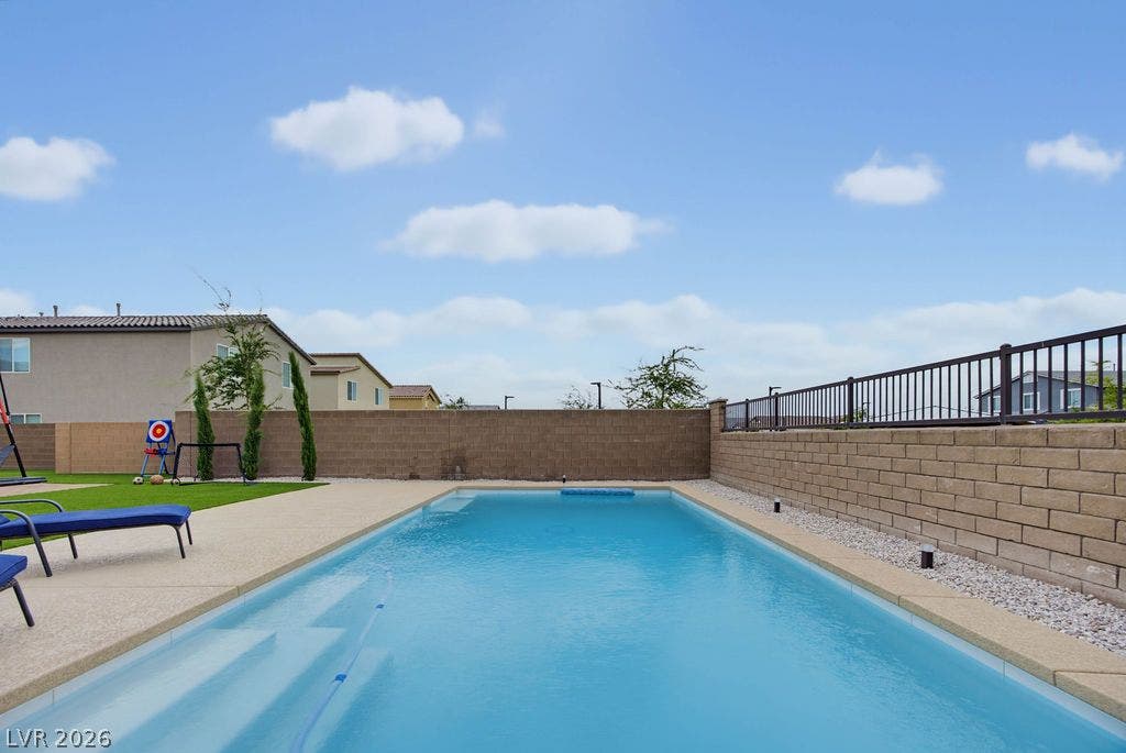 A sparkling swimming pool anchors the backyard, framed by masonry walls and wrought iron fencing.
