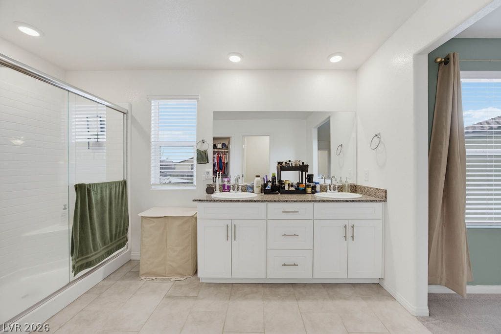 Double vanities with granite counters and a glass-enclosed shower highlight this tiled bathroom.
